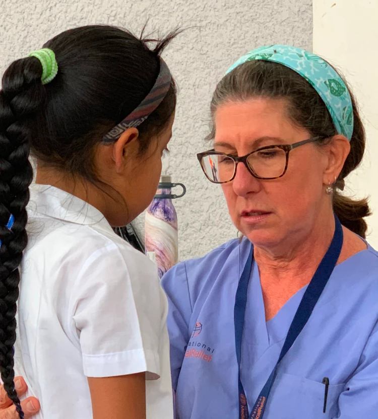 A physician on a medical mission examines a child wearing a school uniform.